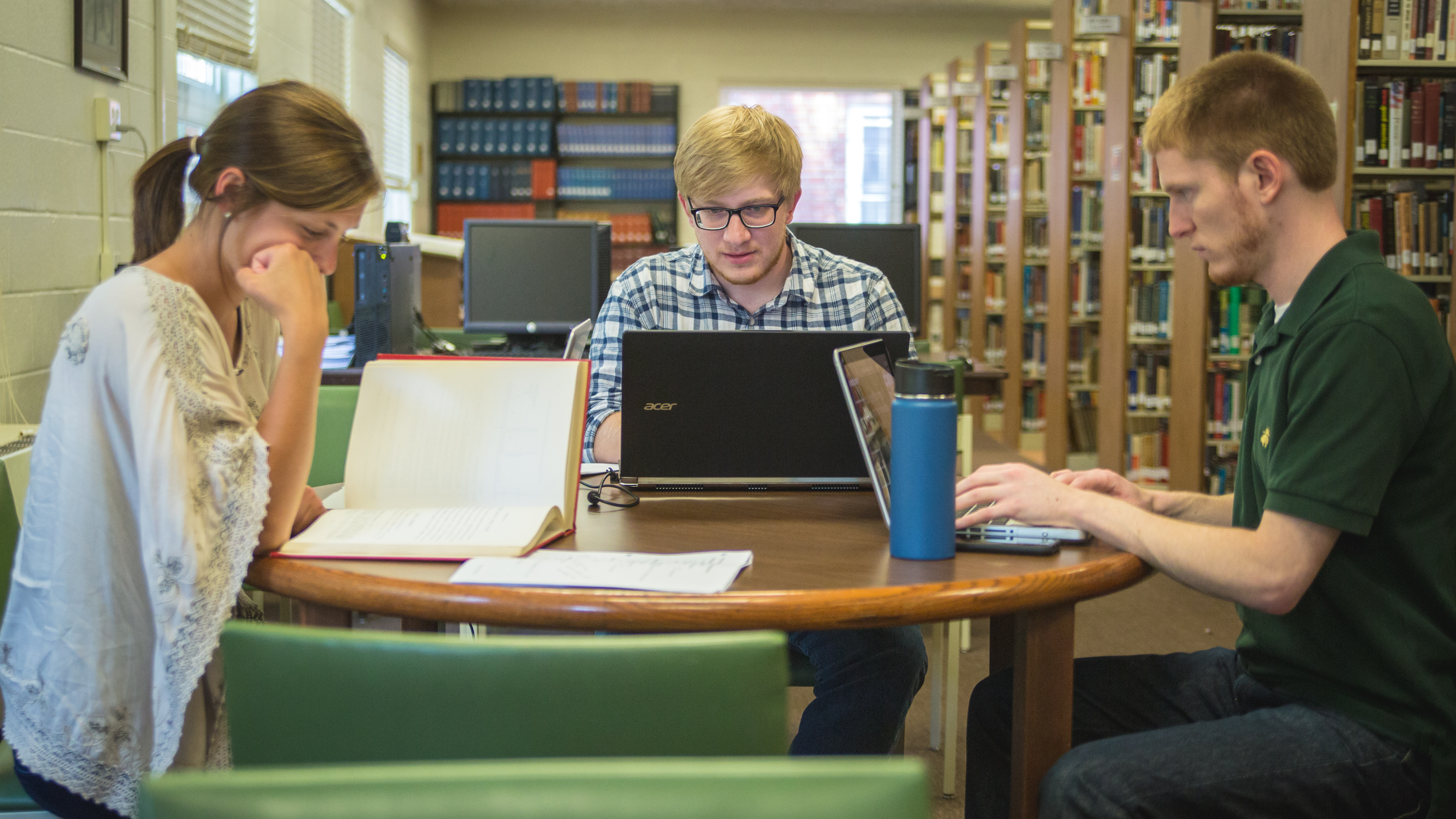 People at a table reading a book or on devices